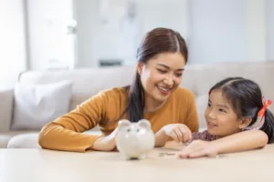 Young mom and child putting money in a piggy bank