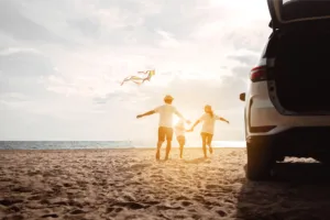 Car on beach with family of three flying a kite