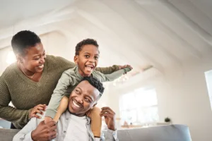 Family of three in living room. Dad is giving the little boy a ride on his shoulders