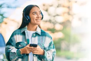 Woman with headphones smiling while holding her phone